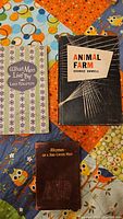 Three books (Animal Farm, What Men Live By, Rhymes of a Red Cross Man) arranged on patterned cloth