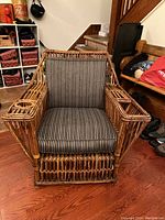 Front view of the 1940s rattan armchair showing the overall design, cushion pattern, and built-in holders on armrests.
