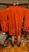 Back view of kimono worn, showing vibrant orange side with white floral embroidery along sleeves and hem.