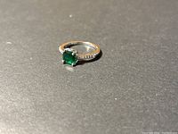 Close-up front angle of the sterling silver ring with green square-cut gemstone set in the center, showing side clear accent stones on band.