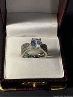 Sterling silver ring in cushioned jewelry box showing front view with large clear center stone and pave diamond-like band.