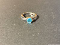 Front angle view of sterling silver ring with oval blue stone and accent stones on band