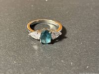 Front angled view of sterling silver ring with blue oval stone and clear side stones on gray surface.