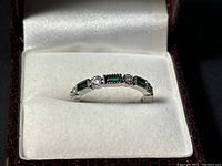 Close-up view of the ring showing the emerald and diamond stones in their settings in white box lining.