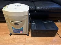 Royal crosscut paper shredder and Canon printer side by side on a wooden floor in front of a couch.