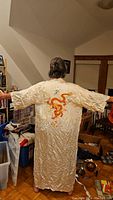 Full back view of cream silk kimono with large embroidered orange dragon design, showing fabric length and texture.