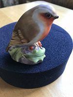 Close-up photo of Royal Worcester robin bird figurine showing brown and white feathers, detailed eyes, red breast, and green leafy base.