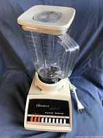 Photo of the vintage Osterizer Galaxie blender showing the base unit with labels and a clear measuring pitcher attached, along with the plug.