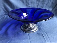 Blue glass bowl with a wide, flared rim and deep blue color on a decorative pewter base.