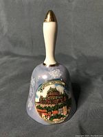 Front view of the lusterware porcelain collector bell showing Chateau Frontenac, Quebec design and floral motifs on lavender surface, with white handle featuring gold-tone accents.