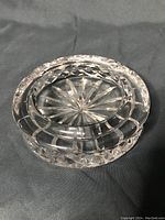 Clear cut crystal ashtray with starburst and diamond-cut patterns on a dark background, showing the solid and heavy nature of the piece.