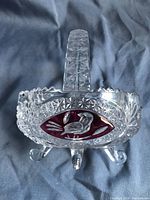 Front view of the clear lead crystal handled bowl displaying the red enameled bird design and tripod feet.