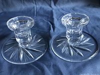 Pair of clear crystal taper candle holders with pinwheel etched pattern on round bases, shown from side view