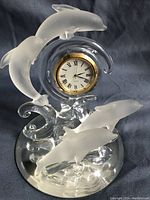 Front view showing four frosted dolphins surrounding circular clock face with gold-tone bezel on a mirror base.