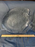 Photo of a clear glass serving platter shaped like a fish, showing textured fish scale pattern and fins, approx. 10.5 inches wide with ruler for scale.