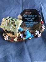 Photo of the ceramic friendship figurine showing a green-roofed birdhouse, two blue birds, pink flowers, and a reflective surface with a friendship poem in blue text.