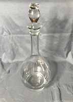 Glass decanter with stopper standing against a plain backdrop, showing the rounded body and stopper.
