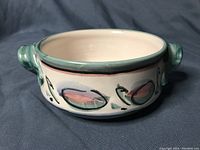 Front view of the round ceramic bowl showcasing green handles and painted blue and pink design on white background.