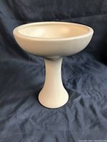 Full front view of white cream standing Haeger pottery pedestal bowl on dark fabric background.