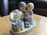Front and side view of the Precious Moments anniversary figurine featuring the couple and snow globe.