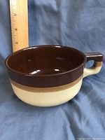 Set of three retro stoneware soup bowls arranged with one bowl closest to the camera, showing the two-tone brown and beige glaze and the bowl's handle. A ruler is placed adjacent for size reference.