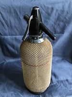 Front view showing the textured gold-coloured metal mesh covering over the glass body and black plastic head with dispensing lever and spout.