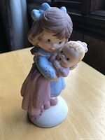 Front view of the Unesco porcelain figurine showing two sisters, the older holding the younger in embrace, pastel dress colors and bows visible.