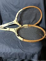Two vintage wooden tennis rackets placed on a dark surface, showing the full racket heads and part of the handles.
