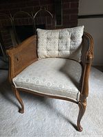 Antique wooden armchair with beige patterned upholstery. Includes curved legs and cane sides.