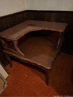 Full angled view of wooden two-tier antique side table showing top and lower tier with scalloped edges and carved legs.