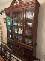 Front view of the large antique wooden china cabinet with glass doors showing contents inside and lower drawers.