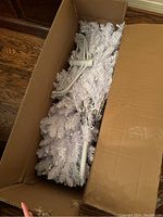 Open box showing white artificial Christmas tree branches and tree stands inside original packaging.