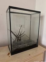 Front view of rectangular glass fish tank aquarium showing black sand substrate, natural wood decoration inside, and ornamental rock.