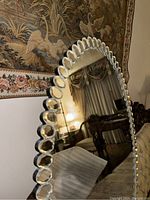 Close-up angled view of the oval mirror showing decorative beveled glass petal segments around the edge and partial reflection of room furniture.