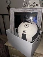 Photo of a Wilson volleyball placed inside a white box beside a decorative framed glass box.