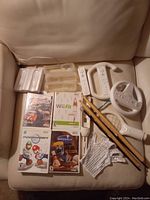 Photo showing Wii game discs, controllers including steering wheel and Nunchuk, Wii Fit balance board, and glove accessory laid out on a chair