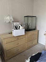 Full view of light wooden dresser with decorative items on top in a corner of a carpeted room.