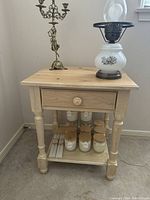 Front view of the wooden nightstand showing drawer, four turned legs and lower shelf with several candles and jars stored.