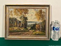 Full view of framed oil on board landscape painting next to water bottle for size reference