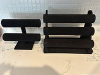 Photo showing two black velvet bracelet display stands side by side on a white marbled surface, one smaller with two fixed bars, the other larger with three removable bars.