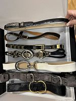 Top view of seven vintage belts arranged in a tray showcasing different materials, buckles and colors.