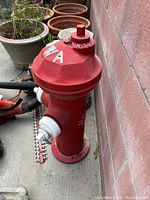 Photo of a red painted cast iron fire hydrant against a brick wall, two white outlet caps, and chains attached; marked 'IOWA' on top dome.