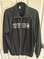Front view of black WWDC track jacket with zipper and logo