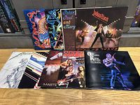 Eight vinyl album covers laid out on wood surface showing assorted rock titles