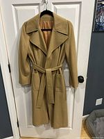 Front view of tan camel hair and wool blend ladies coat on hanger showing full length, collar, belt, and pockets