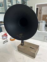 Front view of large black metal gramophone horn on wooden base, showing 'Gramophone Acoustically Amplified Sound' text and gold-toned plaque.