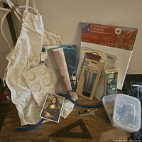 Photo showing white artist apron, clear plastic paint palette, rulers, stencil paper, sketch pencils, and canvas box