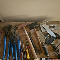 Tools laid out on flat surface showing variety and detail of individual hand tools including wrenches, screwdrivers, mallets, saw, and staple gun