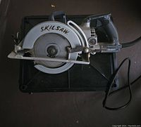 Skilsaw circular saw placed on a black surface, showing the saw's blade and handle clearly.