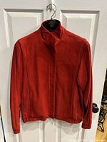 Front view of the ladies red suede jacket hanging on door, showing zipper closure and elasticized bottom